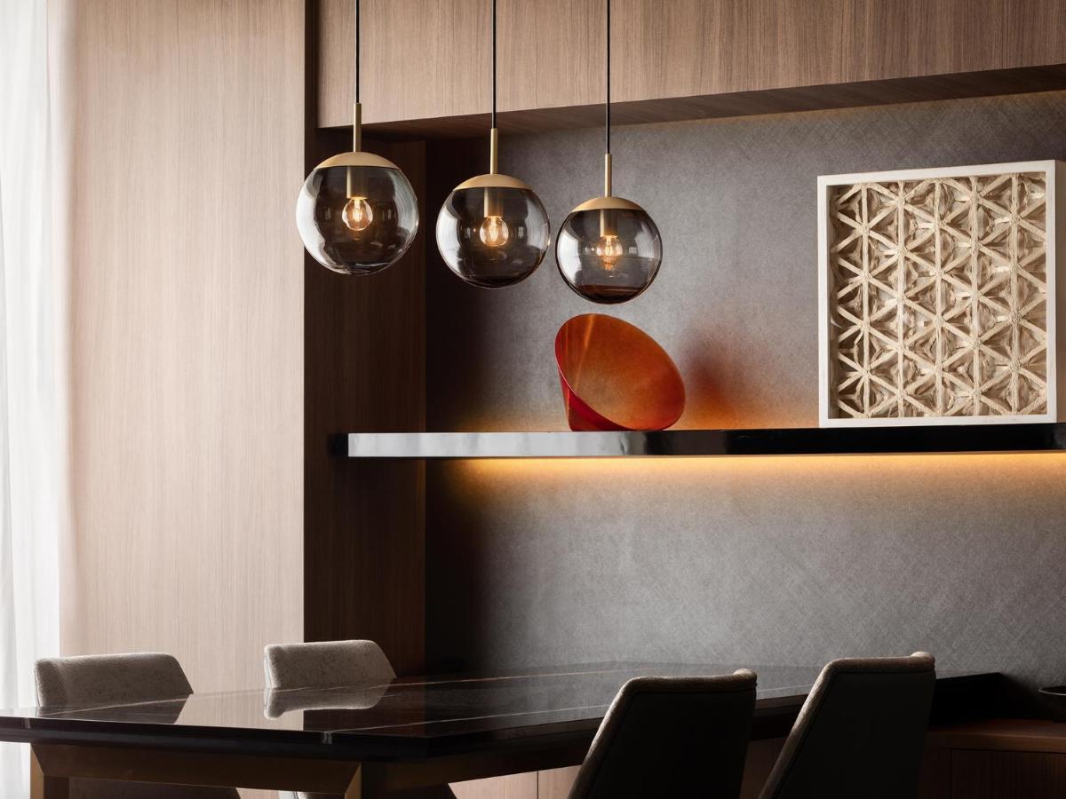 Mitsui Garden Hotel Roppongi Tokyo Premier Eksteriør billede The photo depicts a modern interior design scene. It features a sleek dining area with a dark wooden table and comfortable chairs. Above the table, there are three pendant lights with glass shades that provide ambient lighting. A geometric art piece 