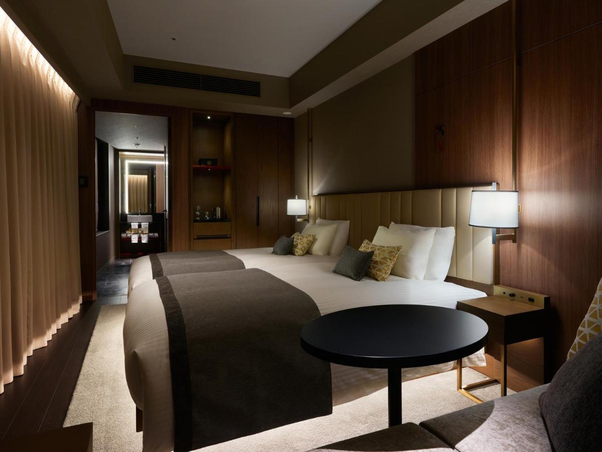 Mitsui Garden Hotel Roppongi Tokyo Premier Eksteriør billede The photo shows a stylish hotel room featuring two beds with plush bedding and decorative pillows. The walls are made of wood, creating a warm and modern atmosphere. There are bedside lamps on each side of the beds providing soft lighting. A small ro