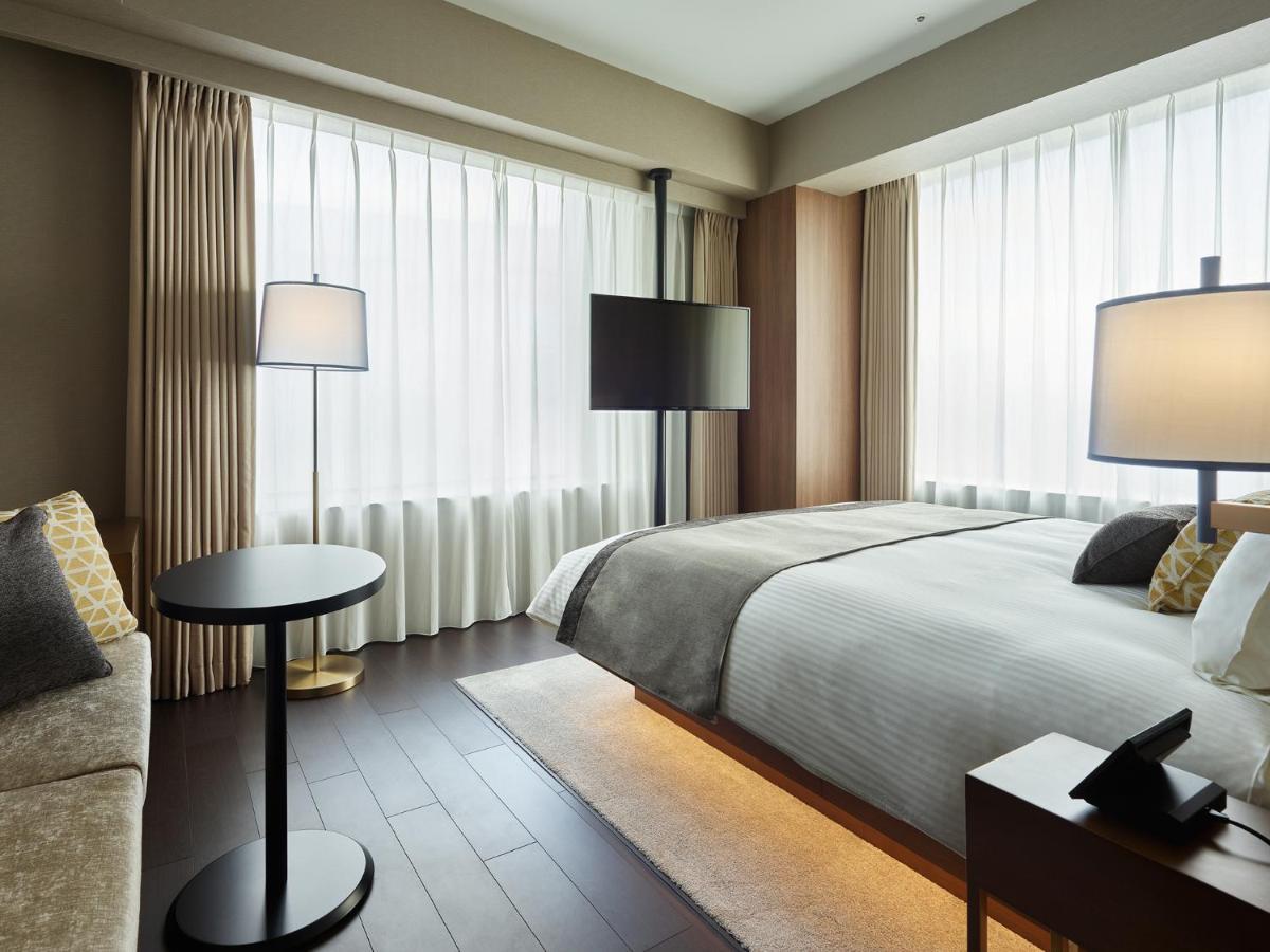 Mitsui Garden Hotel Roppongi Tokyo Premier Eksteriør billede The photo shows a modern hotel room with a contemporary design. It features a large bed with crisp white linens, sitting against a wall with floor-to-ceiling windows covered by sheer curtains, allowing natural light to filter in. To the side, there's