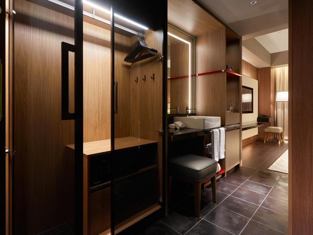 Mitsui Garden Hotel Roppongi Tokyo Premier Eksteriør billede The photo depicts a modern and stylish hotel room's closet area. It features wooden cabinetry with a sleek finish, including mirrored doors. Inside, there are hangers for clothing and hooks mounted on the wall. A small bench or chair is positioned ne