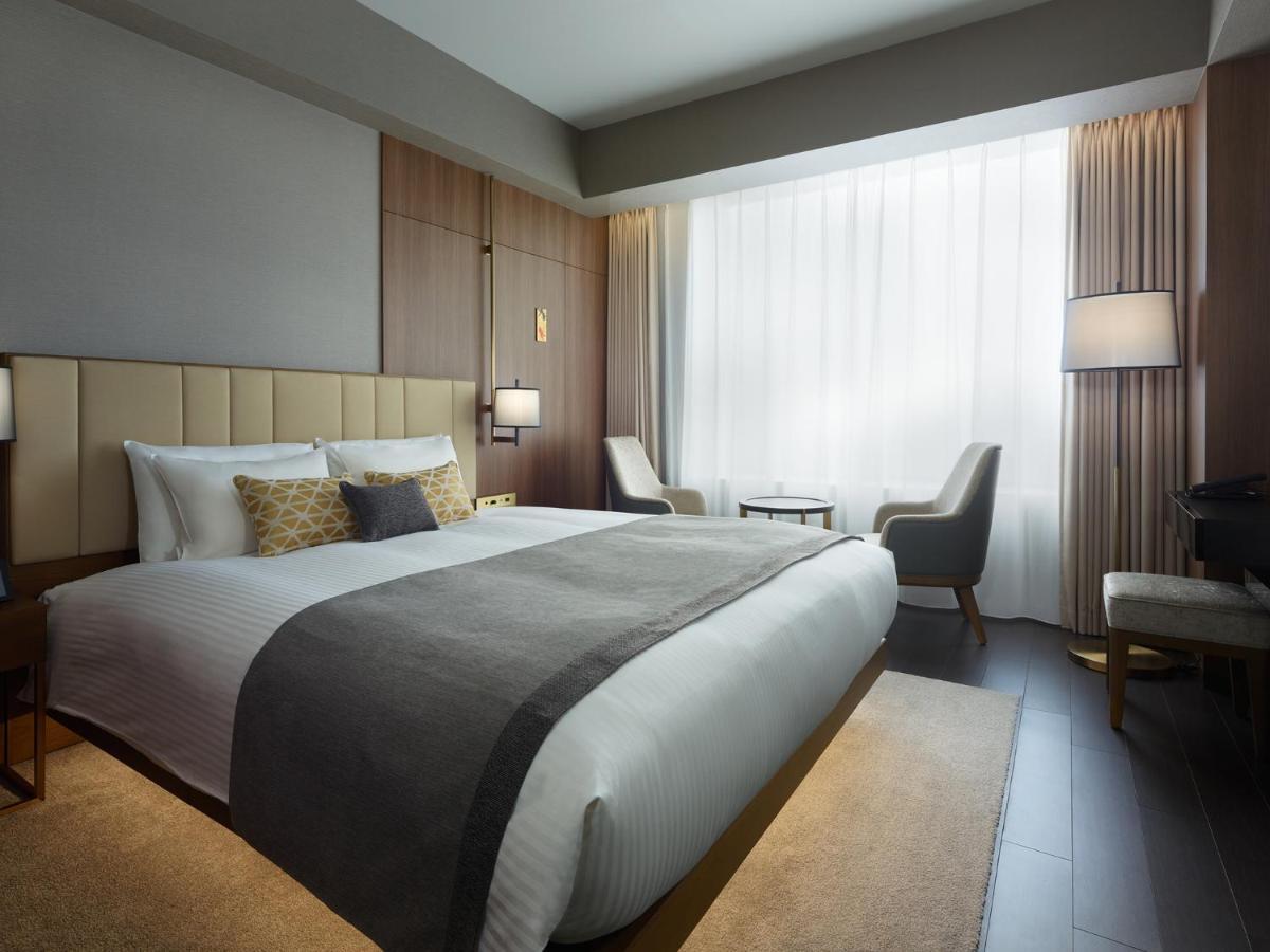 Mitsui Garden Hotel Roppongi Tokyo Premier Eksteriør billede The photo shows a modern hotel room featuring a large bed with a neatly arranged white and gray bedding. The headboard is upholstered in a light color, adding to the room's contemporary design. On either side of the bed, there are bedside lamps provi