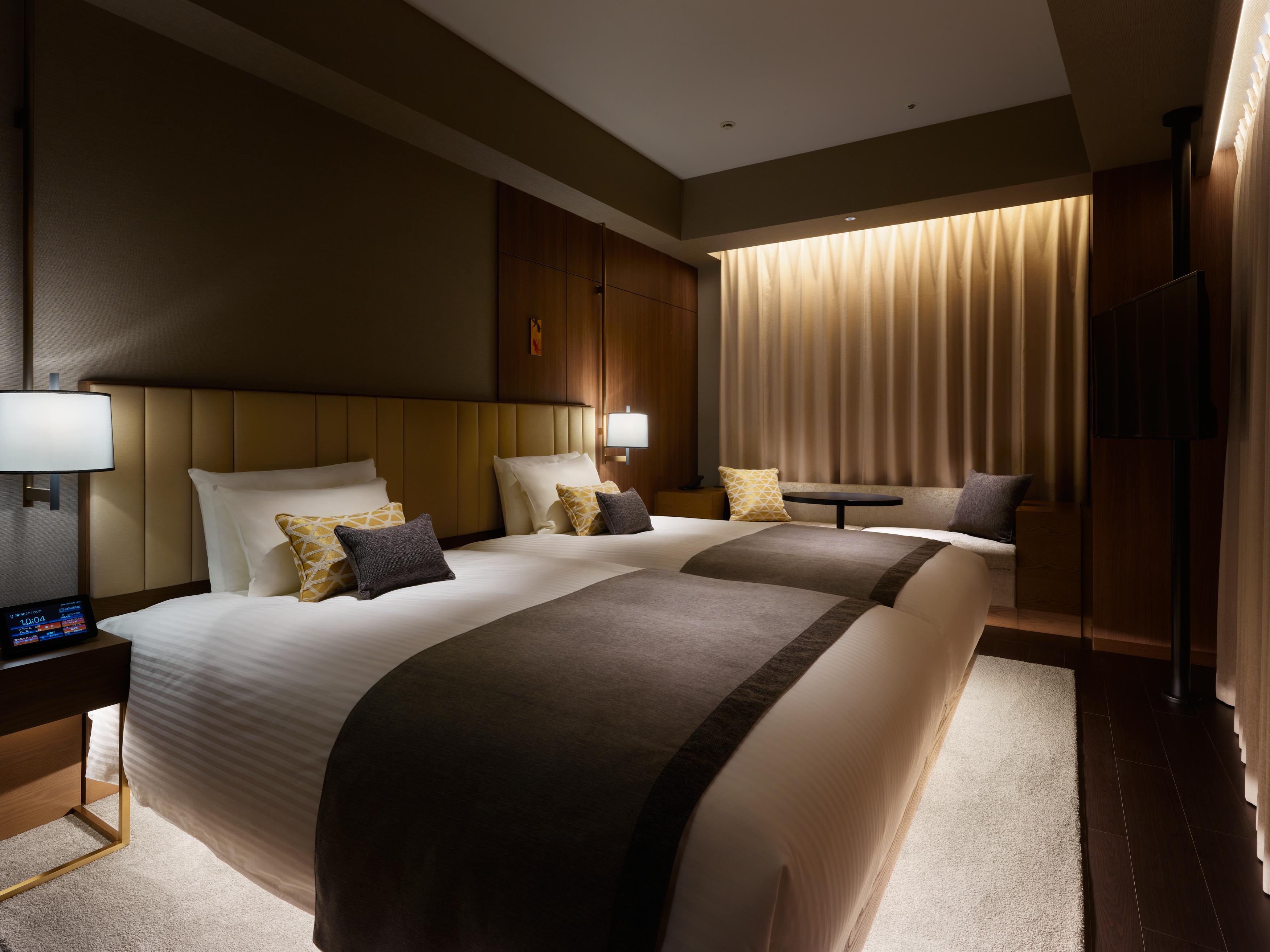 Mitsui Garden Hotel Roppongi Tokyo Premier Eksteriør billede The photo shows a modern hotel room featuring two beds with plush white linens and decorative pillows. The room has a warm and inviting ambiance, highlighted by soft lighting from lamps and the backlit curtains. There is also a small table with chair