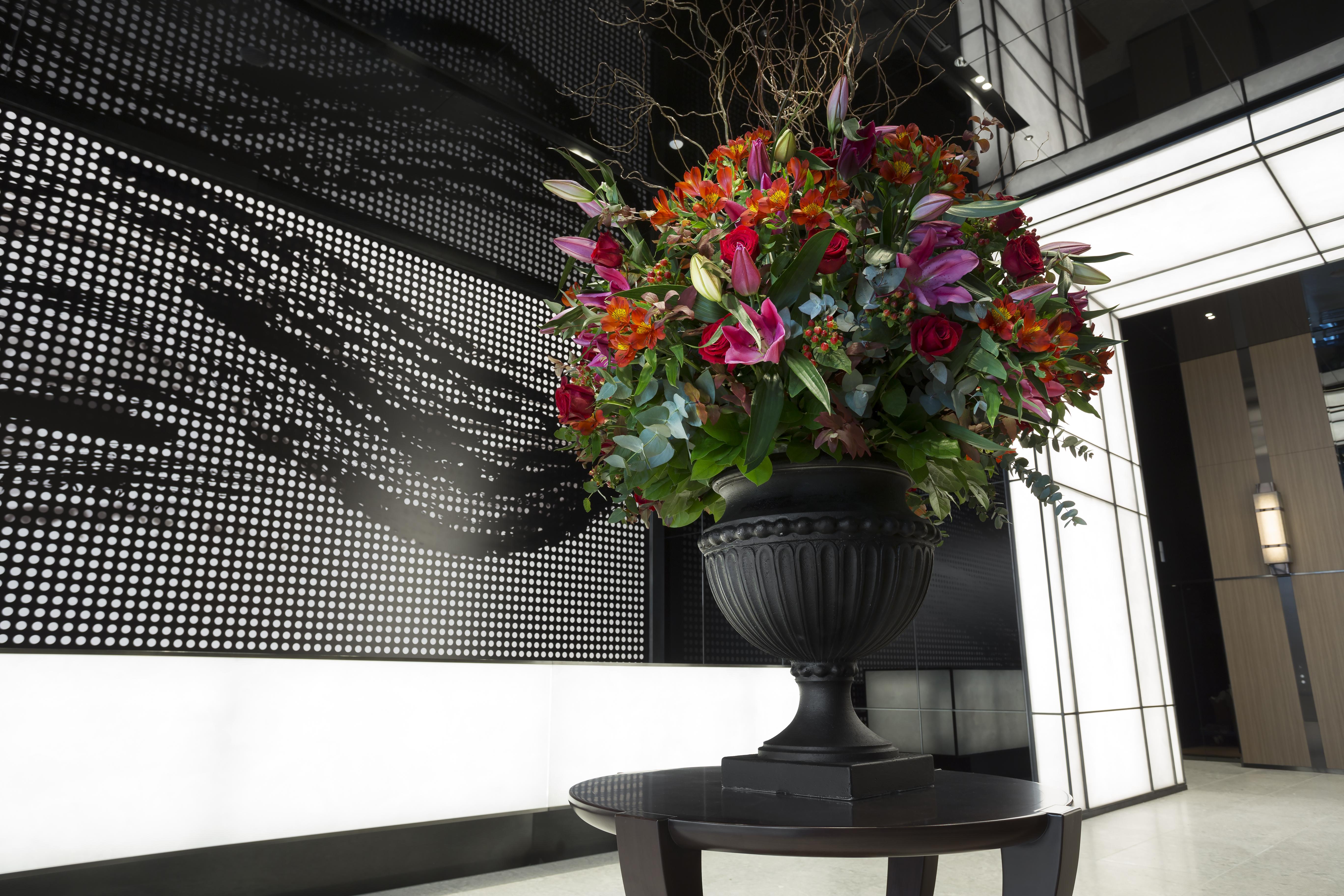 Mitsui Garden Hotel Roppongi Tokyo Premier Eksteriør billede The photo features a large, vibrant floral arrangement in an ornate black urn. The arrangement is composed of various colorful flowers and greenery, showcasing shades of red, pink, orange, and green. This floral display is positioned on a small table