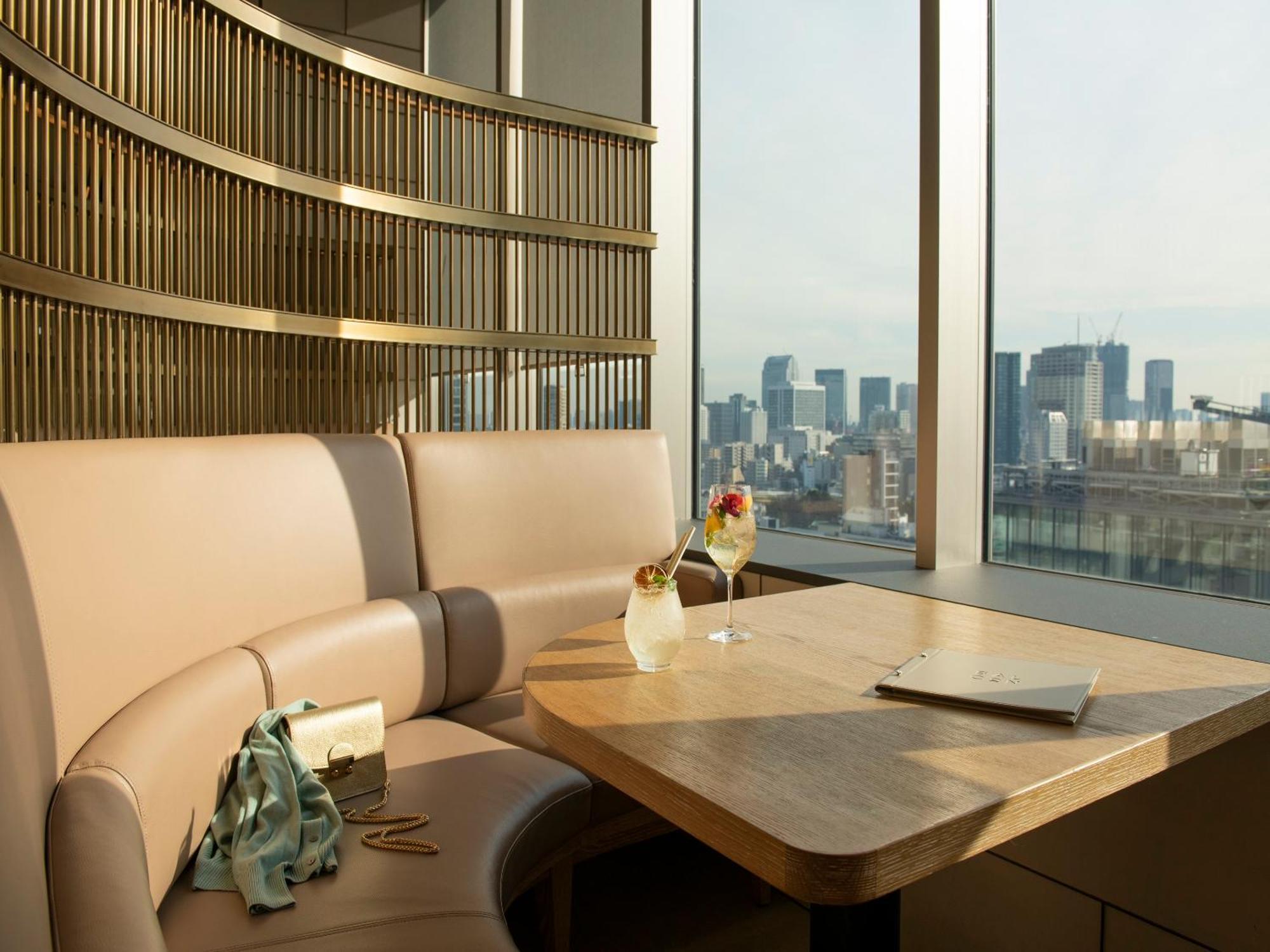 Mitsui Garden Hotel Roppongi Tokyo Premier Eksteriør billede The photo depicts a cozy, modern seating area with a curved booth that features soft, pale upholstery. A wooden table is positioned in front of the booth, and on the table, there are two elegant drinks garnished with fruit. The setting has large wind