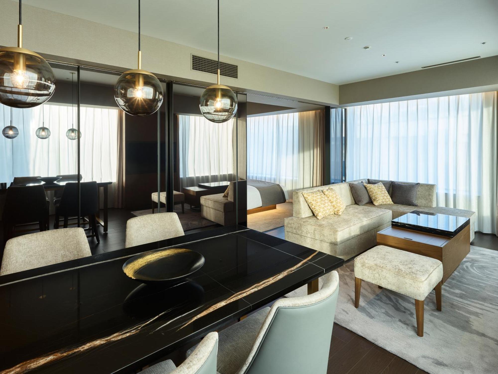 Mitsui Garden Hotel Roppongi Tokyo Premier Eksteriør billede The photo shows a modern and stylish living area. It features a dining table with elegant chairs, a comfortable seating area with a light-colored sofa, and a coffee table. The room is well-lit by large windows draped with sheer curtains, allowing nat