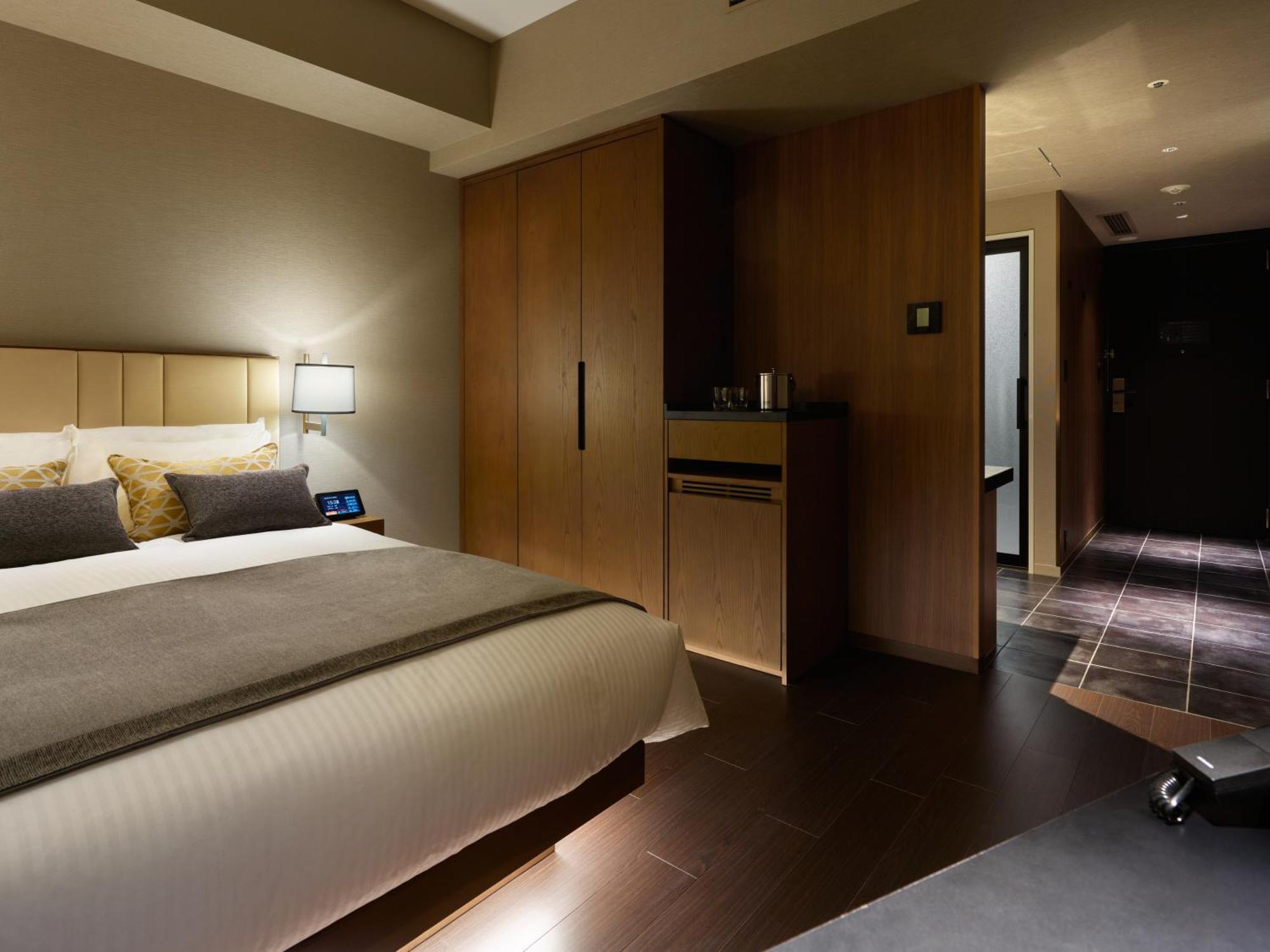 Mitsui Garden Hotel Roppongi Tokyo Premier Eksteriør billede The photo shows a modern hotel room featuring a neatly made bed with decorative pillows. The room has wooden accents, including a wardrobe and cabinetry, contributing to a warm ambiance. A bedside lamp is on one side of the bed, and there's a small a