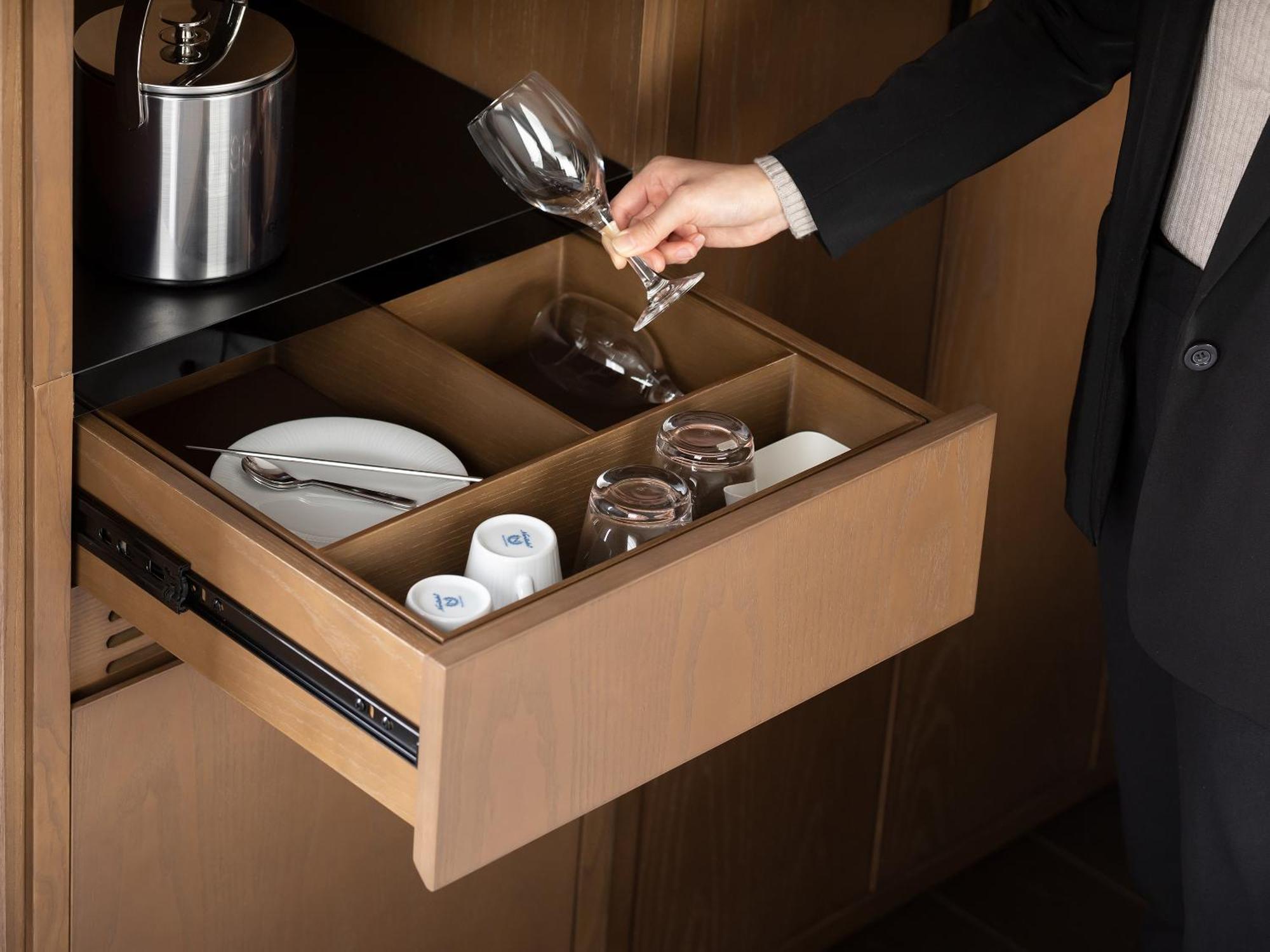 Mitsui Garden Hotel Roppongi Tokyo Premier Eksteriør billede The photo depicts a wooden kitchen drawer being pulled open, revealing a neatly organized selection of dishware. Inside, there are glass cups, a wine glass being held by a person, and plates. The setting appears modern and sleek, with a sophisticated